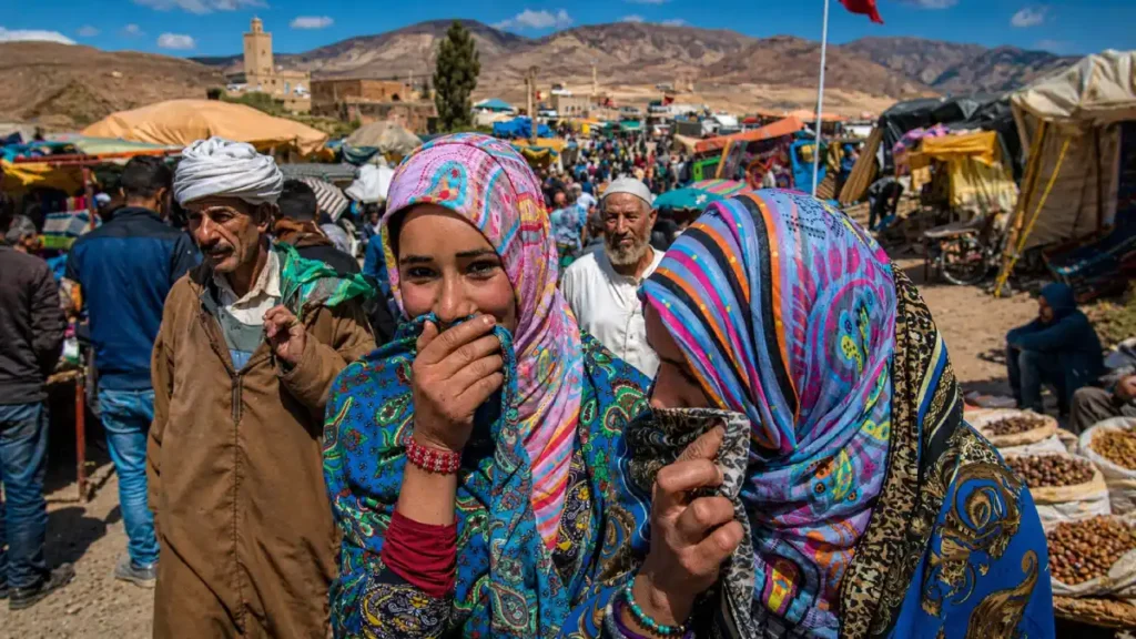 Imilchil Marriage Festival Morocco lively mountain market scene with Amazigh women in colorful scarves, local crowd, market stalls, and Atlas Mountains backdrop during the annual cultural festival