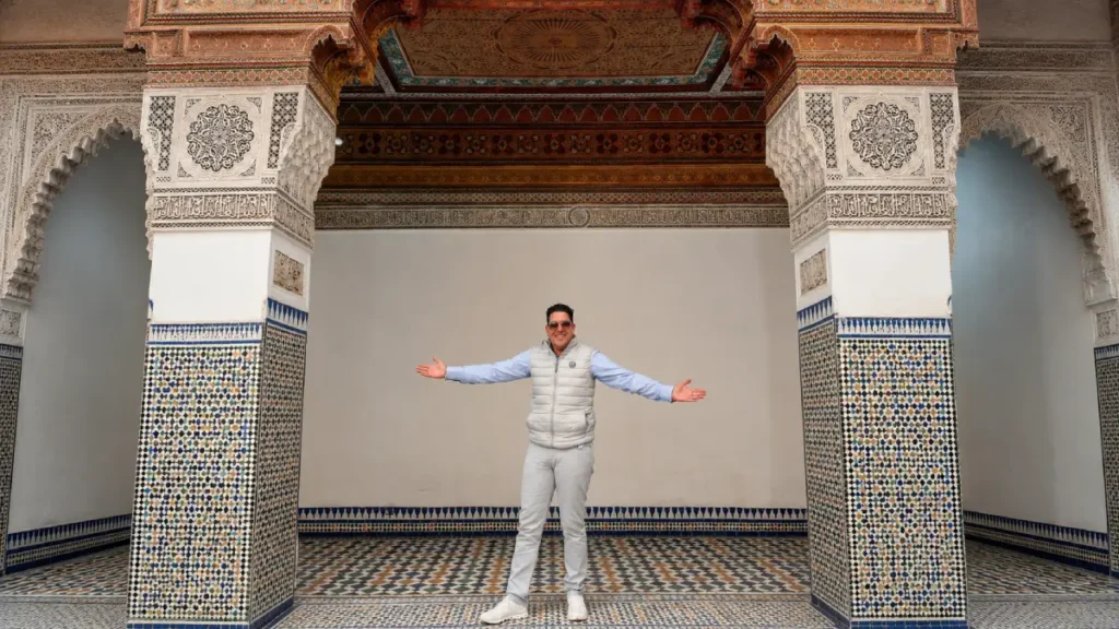 Kamal, a local Morocco guide, standing inside Bahia Palace in Marrakech with zellige tiles, carved plaster, and painted wooden ceiling details