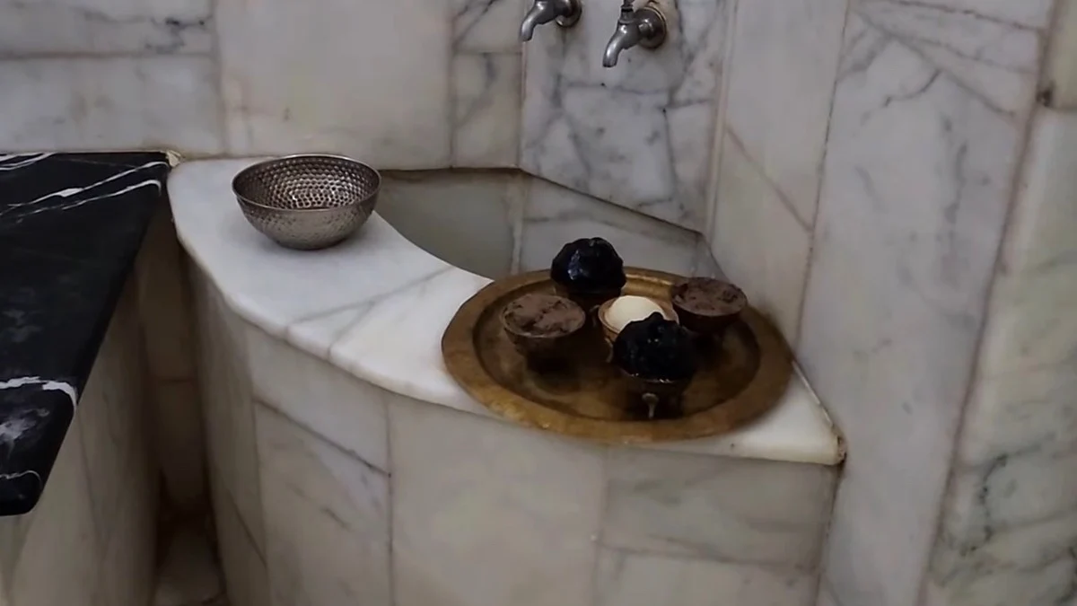 Marble hammam washing area with taps, a metal bowl and a brass tray of treatment bowls