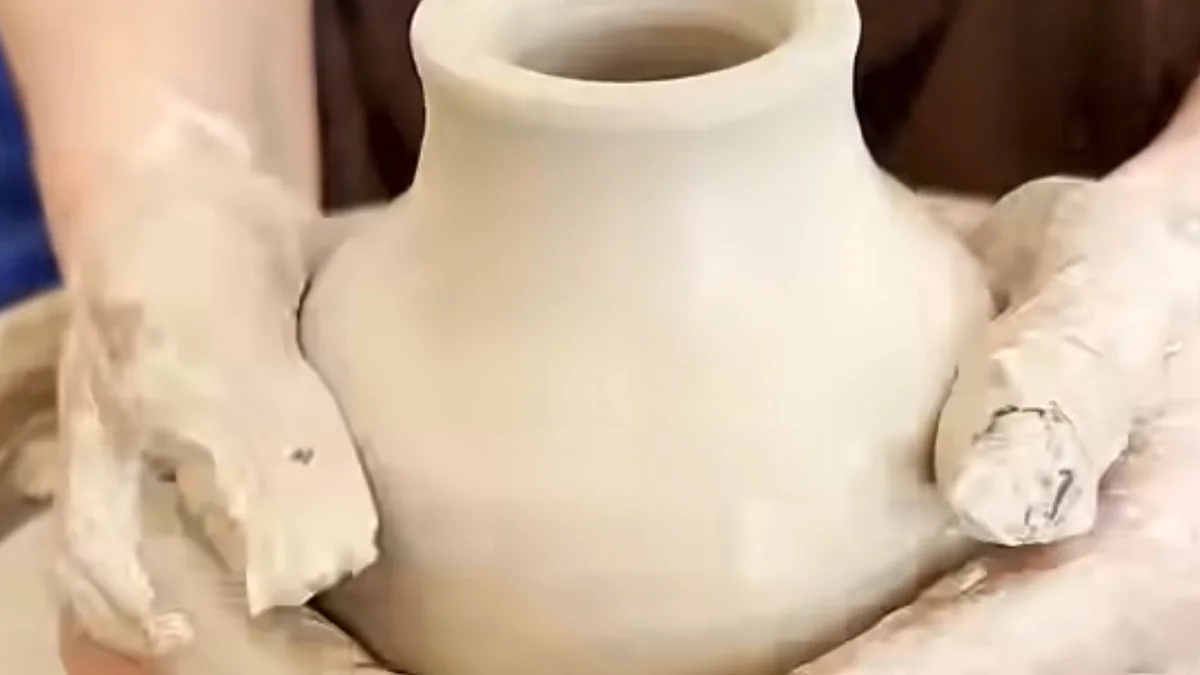 Clay-covered hands holding a small handmade vase