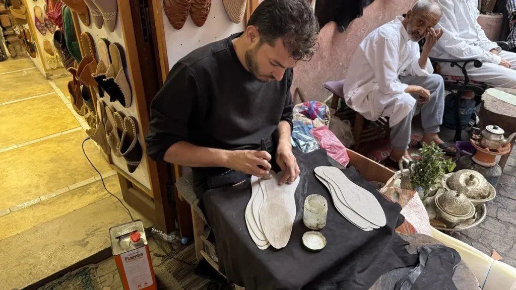 Shoemaker working on footwear components beside a babouche shop in Marrakech
