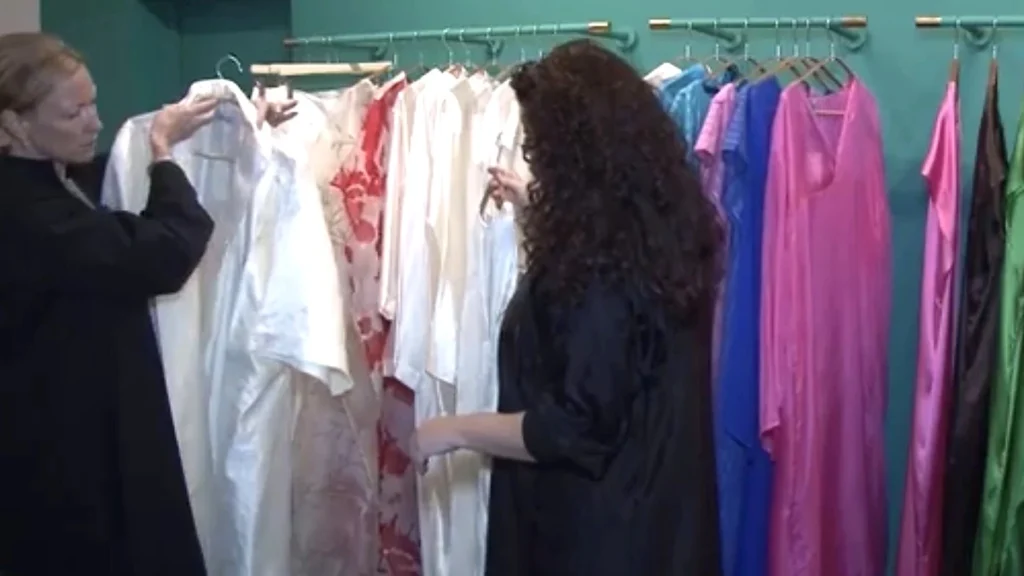 Two women examining a pale garment beside racks of colorful clothing