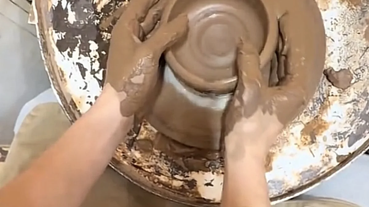 Overhead view of clay-covered hands shaping a bowl on a pottery wheel