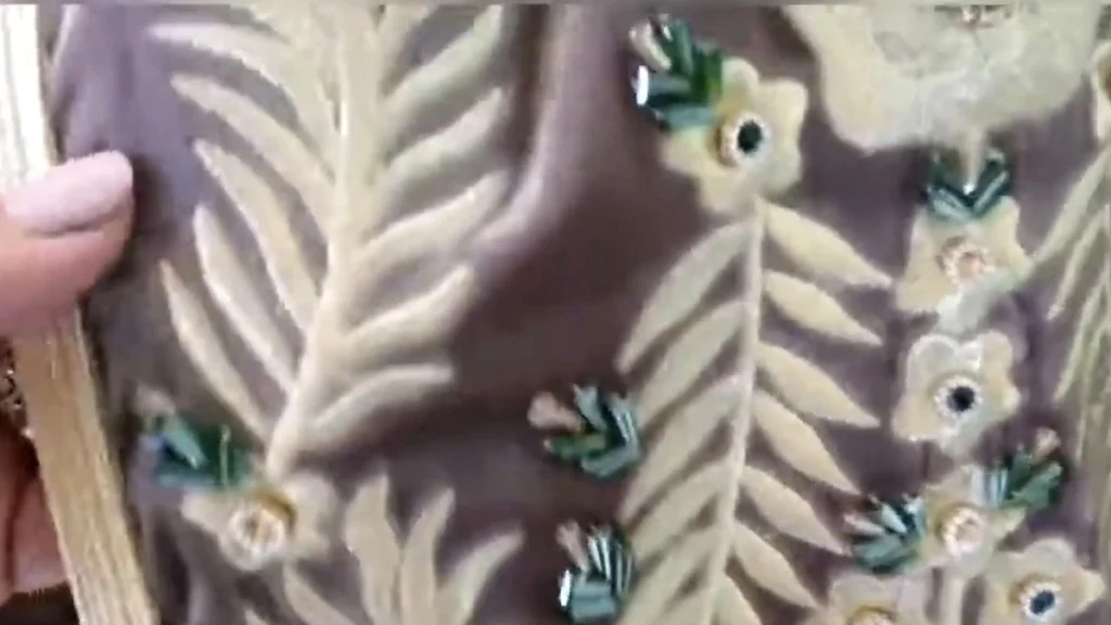Close-up of cream floral embroidery and green bead details on taupe fabric