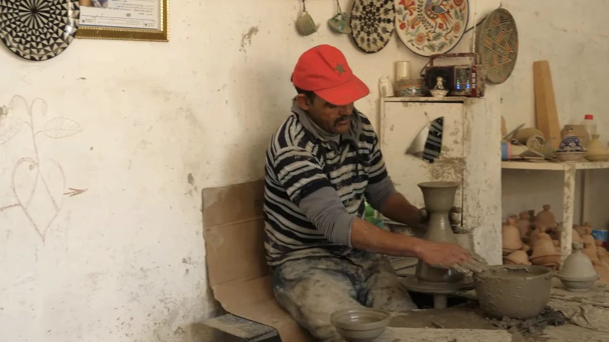 Pottery artisan in a red cap shaping a tall clay vessel on a wheel
